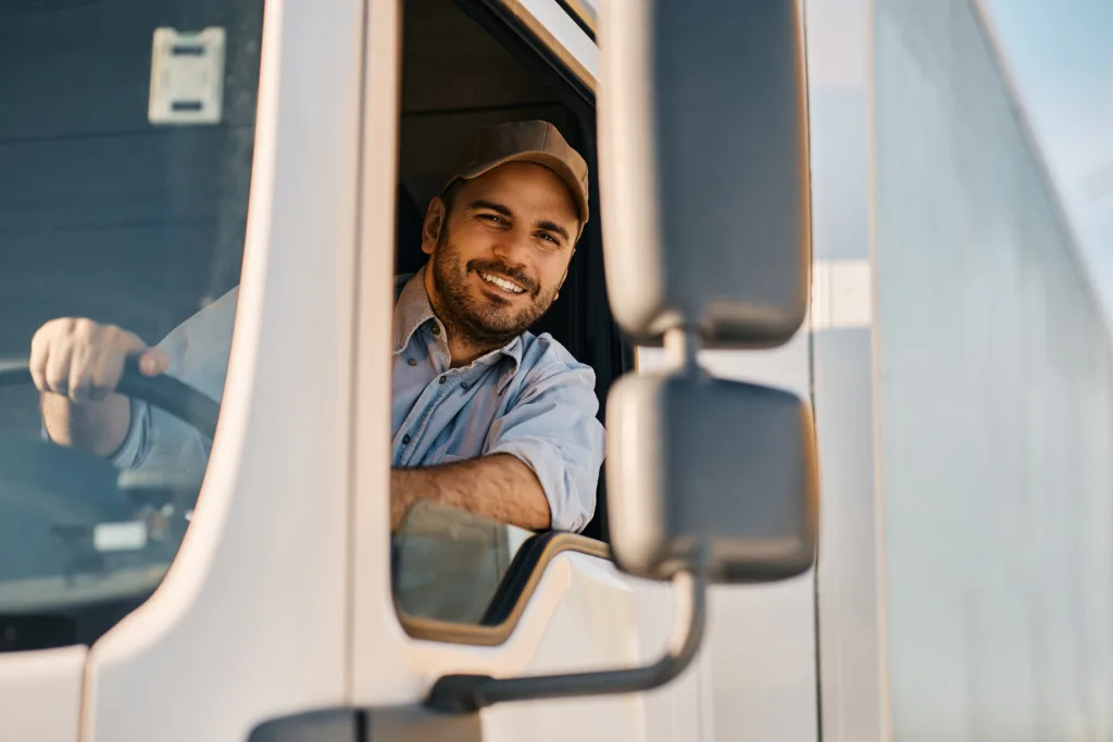 Happy professional truck driver smiling while looking out the window of his truck.
