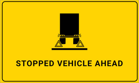 Yellow road sign with a black graphic of a stopped truck, warning triangles, and flashing lights, with the text STOPPED VEHICLE AHEAD below the image.