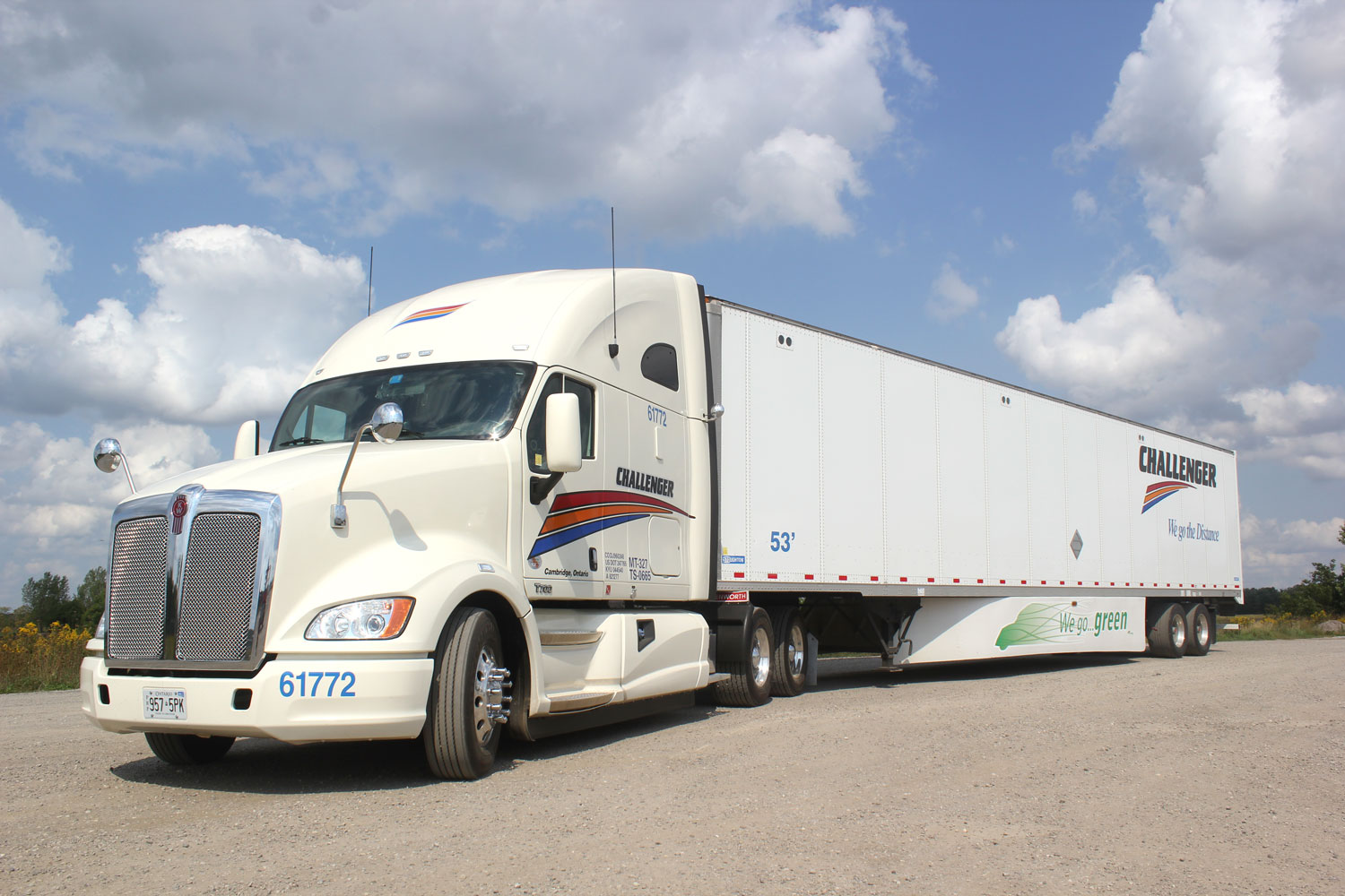 A white semi-truck with Challenger branding and a large trailer is parked on a gravel lot under a partly cloudy sky. The trailer features the slogan driving green and the number 53.
