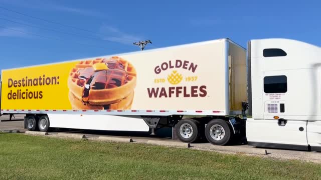 A white RWE semi-truck features a large advertisement on its trailer showing stacked waffles with syrup and butter, with the text “Destination: delicious” and “Golden Waffles” on a yellow background.