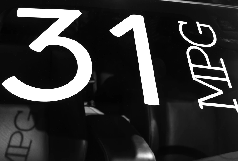Large white numbers 31 and the letters MPG are displayed on a car window, highlighting fuel efficiency—a detail that can support truck driver retention by reducing fuel costs. The background shows a partial view of the cars interior.